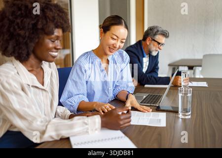 Female partners reviewing contract documents in boardroom during meeting with businessman in the background Stock Photo
