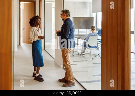 Colleagues discussing project and making decisions while collaborating in professional office corridor Stock Photo