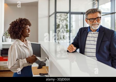 Confident male entrepreneur discussing booking details with female receptionist at hotel front desk in lobby Stock Photo