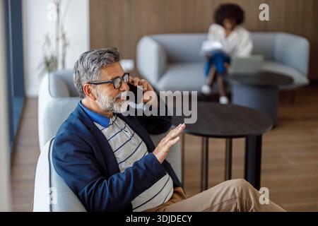 High angle view of bearded professional communicating over mobile phone while sitting on sofa in office Stock Photo