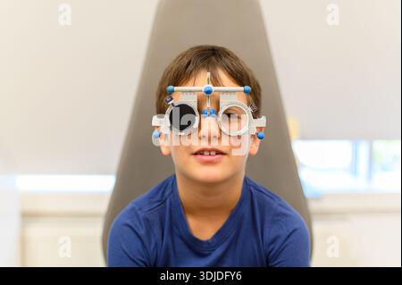 Close-up portrait of boy wearing phoropter undergoing vision assessment during eye examination at ophthalmology clinic Stock Photo