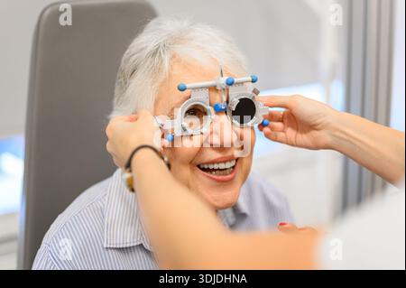 Cropped hands of female ophthalmologist using phoropter to test eyes of smiling senior patient during hospital visit Stock Photo
