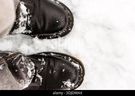 Top view of black winter boots standing on fresh white snow with snow clumps and large copy space. Stock Photo
