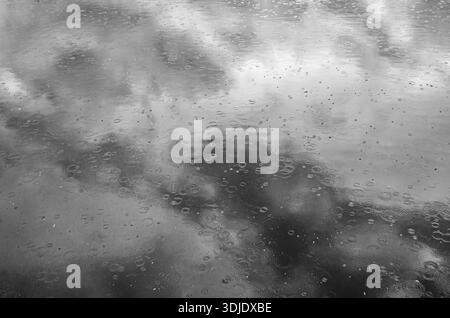 Black and white close-up of raindrops hitting water and forming circular ripples on the surface, creating a moody abstract rainy background Stock Photo