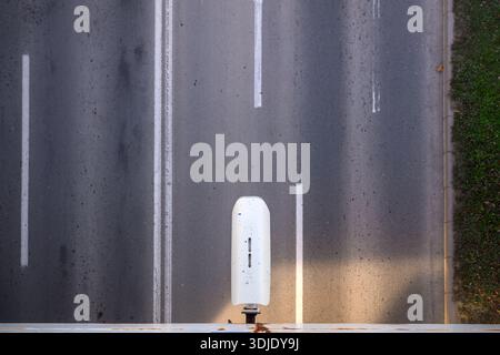 Overhead view of speed camera housing on empty multi-lane road with faded white markings and grass verge. Stock Photo