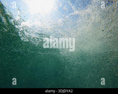 Underwater view filled with air bubbles and sunlight streaming through the surface, capturing the dynamic beauty of the ocean depths. Low angle view. Stock Photo