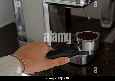 A hand holding the portafilter of an espresso machine, ready for coffee grounds to be added. The image captures a key step in the espresso brewing Stock Photo