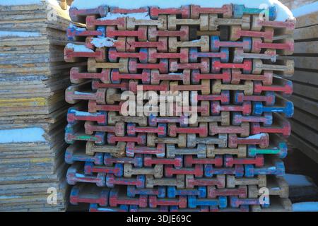 Front-on view of weathered timber panels stacked in a grid, red and blue painted ends visible; snow caps on upper boards; daylight with side shadows. Stock Photo