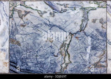 Close-up of aged and textured marble floor tiles featuring intricate patterns of blue and green veins on a white and light grey base, showing signs of wear and time. Stock Photo