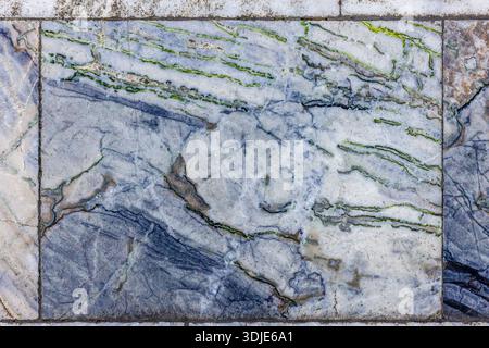 Close-up of aged and textured marble floor tiles featuring wavy green and blue veins on a white and light grey background, showing signs of wear and time Stock Photo