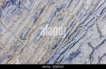 Detailed close-up of aged and textured marble featuring diagonal blue and tan-toned veins on a white and light grey surface, showing signs of wear. Stock Photo