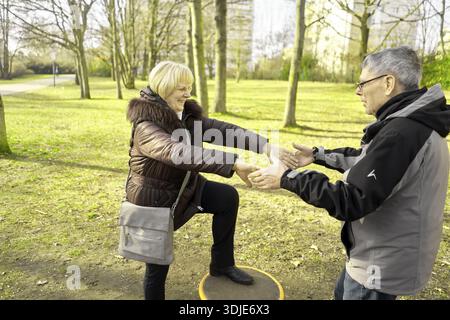 Overjoyed senior couple playfully balancing on turntable wheel, rotation, rotating, turning, interacting in a park, Equilibrioception, activity, activ Stock Photo