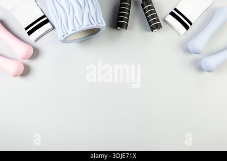 Top view of pink dumbbells, blue dumbbells, blue massage roller, black jumping rope on grey background. White sport socks, fitness, sport, gym. Stock Photo
