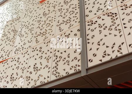 A wall features a pattern of geometric shapes made from cut metal. The unique design adds visual interest to the building. Sunlight highlights the str Stock Photo