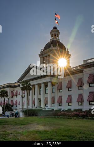 The setting sun explodes in a brilliant starburst behind the dome of Florida's Historic Capitol, casting long shadows across the grounds. This dramati Stock Photo