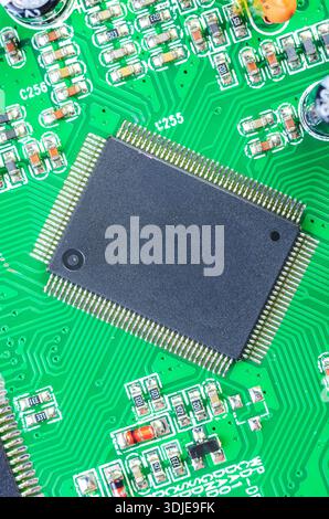 Detailed macro shot showcasing a central processing unit or memory chip with numerous pins connected to a vibrant green motherboard, surrounded by sma Stock Photo