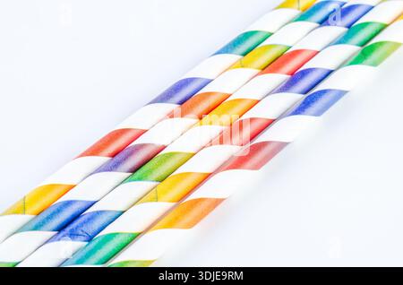 A collection of vibrant, disposable paper straws with rainbow stripes are neatly arranged in a diagonal pattern against a clean white backdrop, perfec Stock Photo