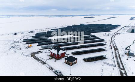 Aerial view of solar panels contrast against the stark white snow-covered landscape, with a small red-roofed building providing a splash of color, Sre Stock Photo