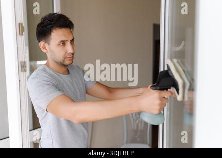 Side view of window cleaner male using squeegee to wash glass of window in an apartment, ensuring streak-free cleanliness and natural light Stock Photo