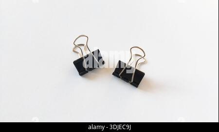 Binder clips on white paper, bulldog clip, black metallic stationery clips arrange isolated on white background. Stock Photo