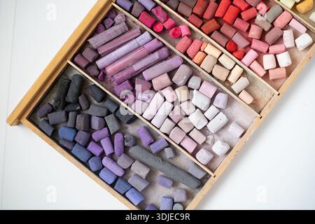 Soft pastels set in wooden box on white table. Drawing material. Art background. Open wooden box of soft pastels close-up view, multicolor art supplie Stock Photo