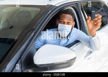 Happy African Man In Medical Mask Sitting In Car And Showing Key Stock Photo