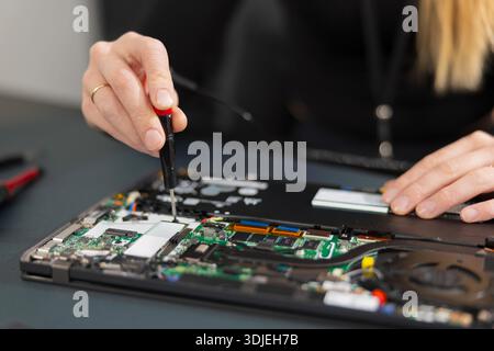 Female IT technician repairs a laptop internals with a screwdriver on a workbench during hardware maintenance and diagnostics Stock Photo