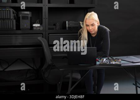 Female IT technician in a server room working on a laptop and diagnosing hardware Stock Photo