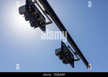 A low angle perspective looking up at two traffic lights suspended from a long curved metal mast arm. The signal heads are silhouetted against the int Stock Photo