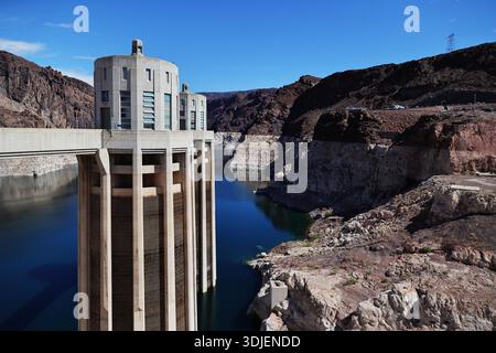 Concrete intake tower at Hoover Dam on the Nevada Arizona border in the USA beside calm blue reservoir water and exposed shoreline bands in daylight. Stock Photo