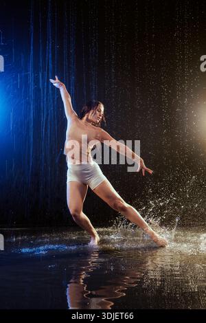 Full-body female contemporary dancer performing in falling rain with water splash and copy space. For website banner or ad promoting dance, fitness, o Stock Photo
