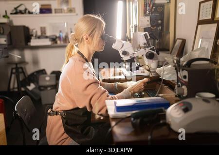 Woman examining intricate details using microscope in workshop Stock Photo