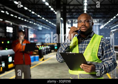 Warehouse technician uses radio communication to guide machinery operation, managing engineering responsibilities for industrial environment. Manpower for manufacturing process. Stock Photo