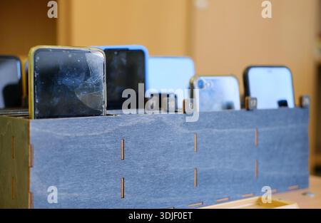 Students' mobile devices are neatly organized in a wooden box, with screens visible, highlighting the restriction on phone usage during class time and Stock Photo