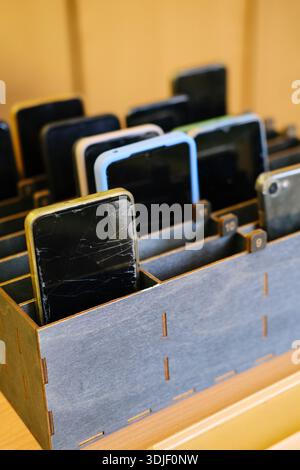 Cell phones are neatly organized in a wooden box, displaying different models and conditions, emphasizing the importance of reducing distractions in e Stock Photo