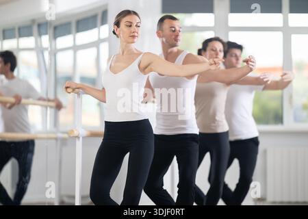Woman practicing demi plie at barre at group ballet class Stock Photo