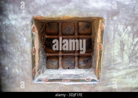 Close up of rusty metal window grate set in weathered steel surface showing corrosion texture and industrial decay. Abstract background with aged meta Stock Photo
