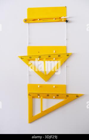 Vertical arrangement of yellow drafting tools, featuring protractor and triangle rulers on a clean white background, emphasizing precision and creativ Stock Photo