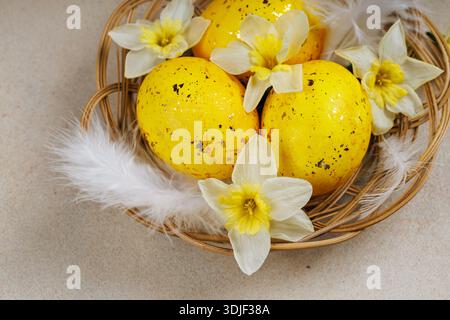 Closeup of yellow Easter eggs with daffodils and feathers in a basket Stock Photo