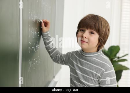 Schoolboy doing math on chalkboard in classroom Stock Photo