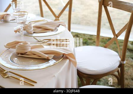 Beautifully arranged wedding banquet table showcases gold-accented plates, elegant napkins, and crystal glassware, enhancing the festive ambiance and Stock Photo