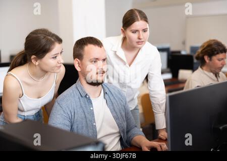 Two female friend companions stands next to computer courses male student Stock Photo