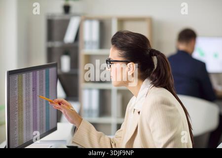Female accountant analyzing financial data on computer monitor in modern office Stock Photo