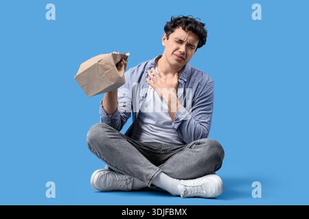Young man with paper bag having panic attack on blue background Stock Photo