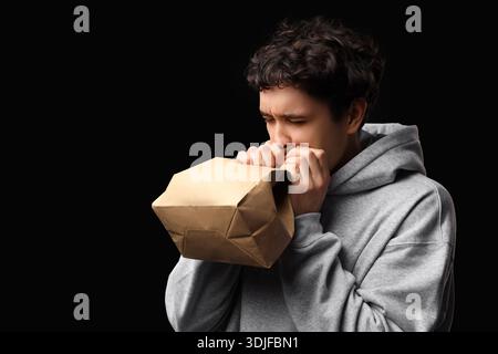Young man with paper bag having panic attack on black background Stock Photo