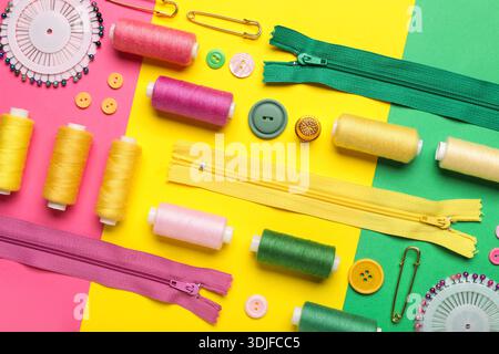 Composition with thread spools, zippers, ball pins and buttons on color background, closeup Stock Photo