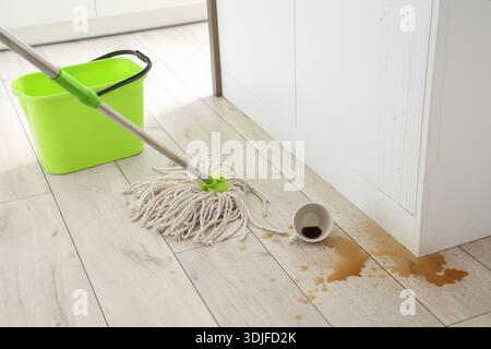 Overturned cup, spilled coffee and mop on floor in kitchen Stock Photo