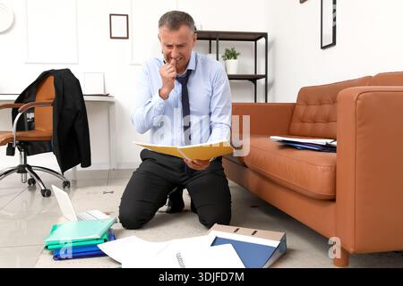Worried mature businessman reading documents while biting nails in office Stock Photo