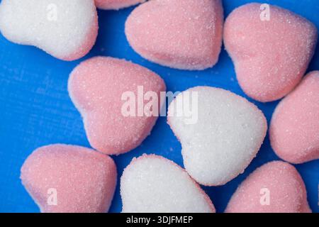 Festive top view of pink and white heart-shaped sweets scattered over a vibrant blue textured background, featuring crystalline sugar details Stock Photo