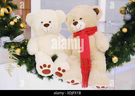 Two cute teddy bears, one light and one dark, are displayed on a decorative wreath with shiny ornaments, creating a joyful holiday atmosphere Stock Photo